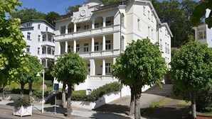A large, white, multi-story building with a prominent clock and balcony railings. - Villa Celia Sellin by Interhome (Ostseebad Sellin)