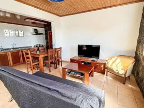 Ein Wohnzimmer mit Sofa, Fernseher, Esstisch mit Stühlen und einer Küchenzeile inklusive Herd und Schränken.