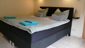 Ein ordentlich bezogenes Bett mit blauen Handtüchern, einem schwarzen Kopfteil und gestreiften Kissen.