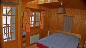 Ein Schlafzimmer in einer Holzhütte mit einem Bett, einem Fenster mit Vorhängen und einem kleinen Tisch.