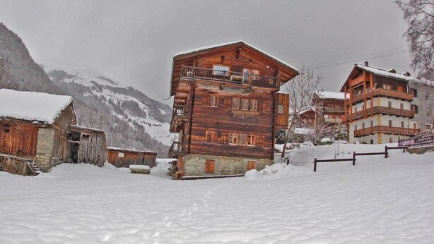 Eine Holzhütte mit mehreren Balkonen, umgeben von schneebedeckten Bergen.
