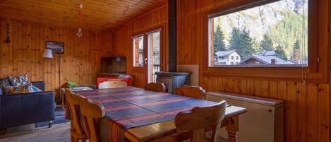A wooden cabin interior with a dining table, chairs, a sofa, and a fireplace.