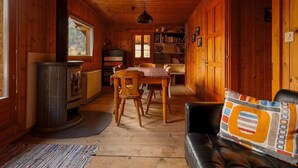 Ein gemütliches Blockhaus-Interieur mit Holzvertäfelung, einem Essbereich, einem Kamin und einer Couch mit einem farbenfrohen Kissen.