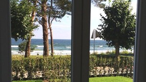 A view through a glass door to a grassy area with trees and a beach in the background. - Villa Seeblick Binz by Interhome (Binz)