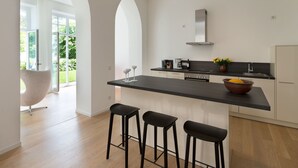 A modern kitchen with a central island, bar stools, and a view of the outdoors through large windows. - Villa Seeblick Binz by Interhome (Binz)