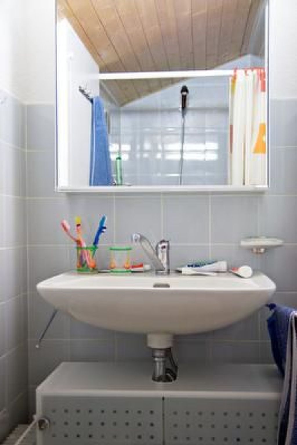 A bathroom with a white sink, a mirror above it, and a shower visible in the reflection.