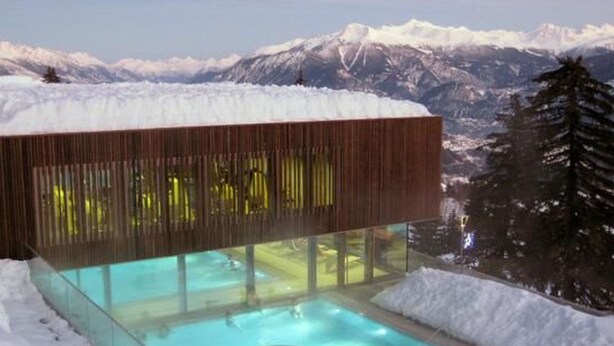 A modern building with a glass pool surrounded by snow, set against a mountainous backdrop. - Ski-in Wohnung in Anzere mit Parkplatz by Interhome (Anzère)