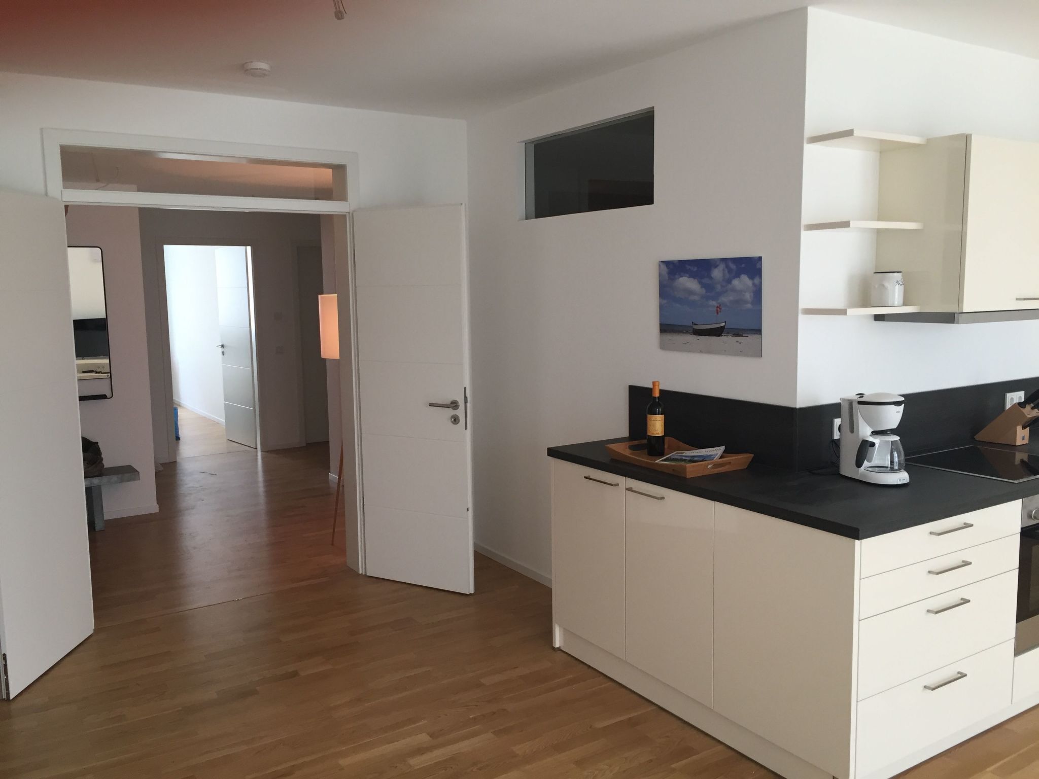 Een moderne keuken met witte kasten, een zwart aanrecht en een fles wijn op het aanrecht.