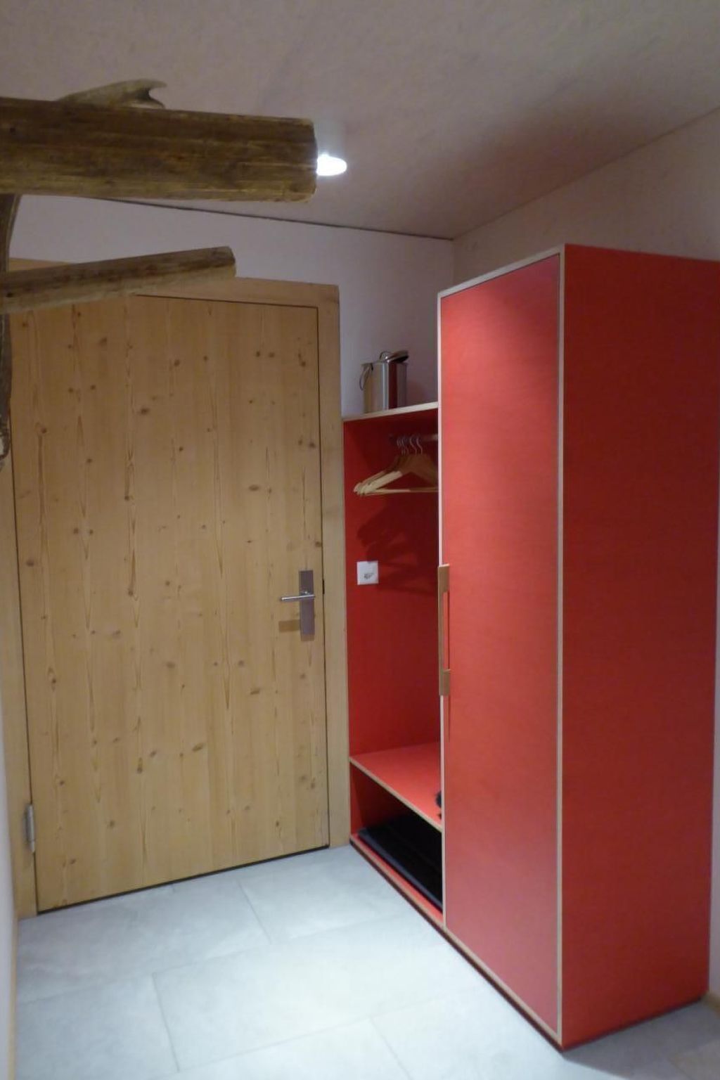 Ein Zimmer mit einer Holztür, einem roten Kleiderschrank und einem Fliesenboden.