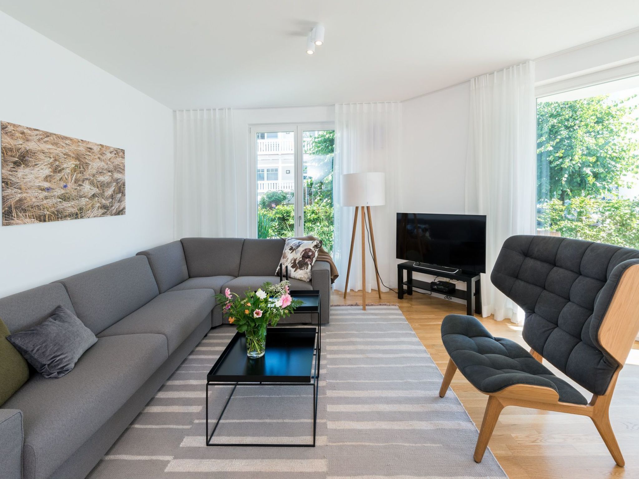 Een moderne woonkamer met een grijze bank, een zwarte salontafel, een zwarte fauteuil, een flatscreen televisie en een vloerlamp.