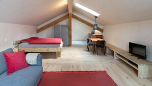 A compact, loft-style bedroom with a wooden ceiling, a bunk bed, a desk with a chair, and a television. - Bijou - BioBergün by Interhome (Bergün)