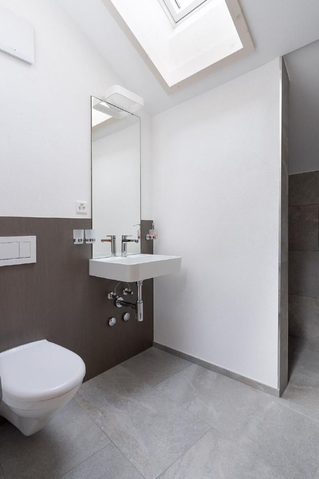 A modern bathroom with a skylight, a white sink, a toilet, and a shower area.