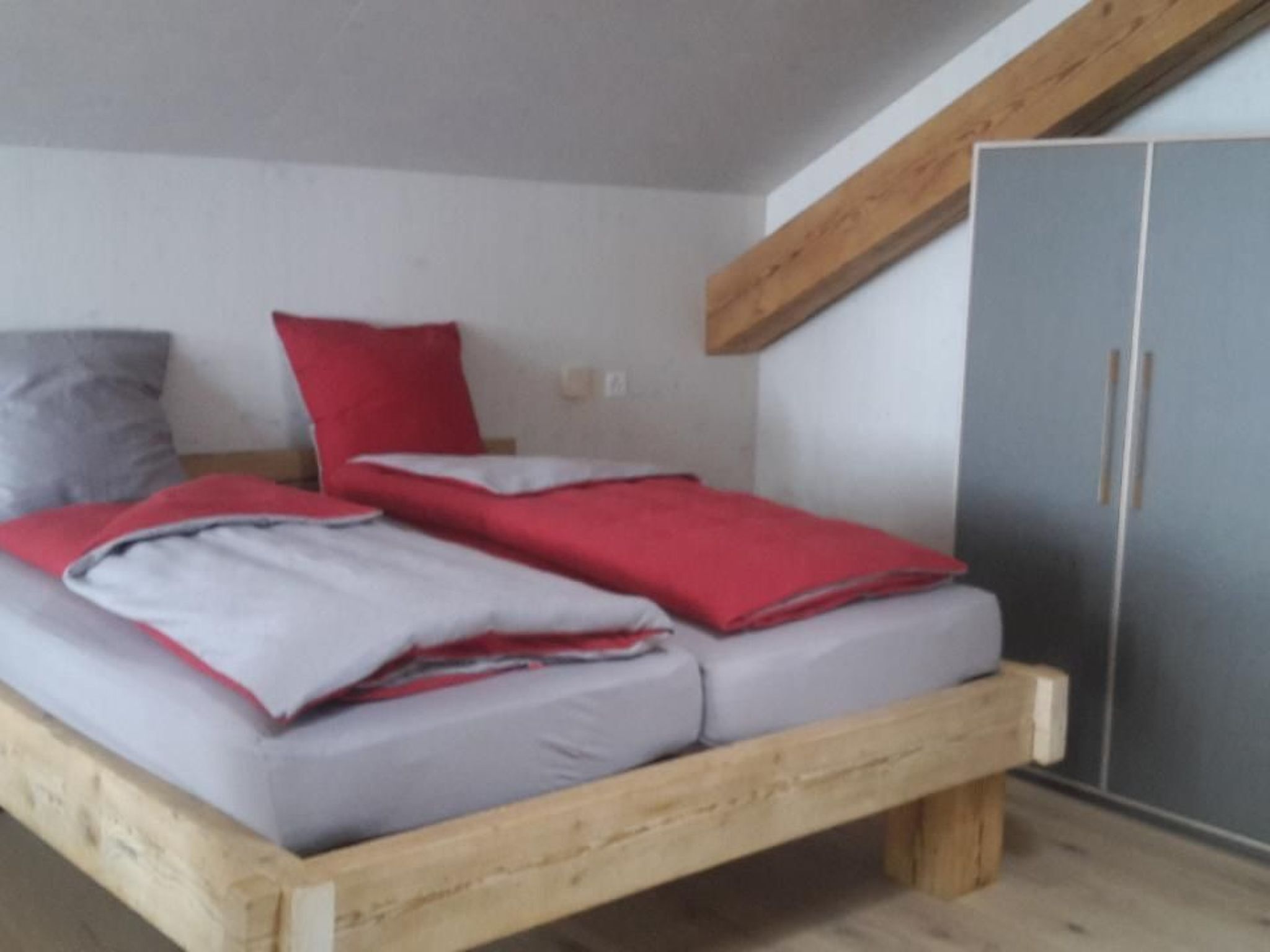 Een slaapkamer met een houten bedframe, twee kussens en een grijze kledingkast.