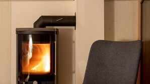 A modern living room with a wood-burning stove, a comfortable armchair, and a view of the outdoors. - Bijou - BioBergün by Interhome (Bergün)