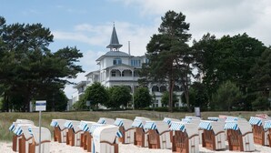 Ein Strand mit mehreren Reihen von Liegestühlen und ein großes weißes Gebäude mit einem Kirchturm im Hintergrund.