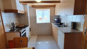 Une cuisine de taille réduite, dotée de meubles en bois, d’une cuisinière et d’une fenêtre qui laisse entrer la lumière naturelle.