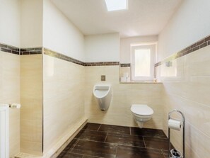 Ein kleines, modernes Badezimmer mit Urinal, Toilette und einem Fenster für natürliches Licht.