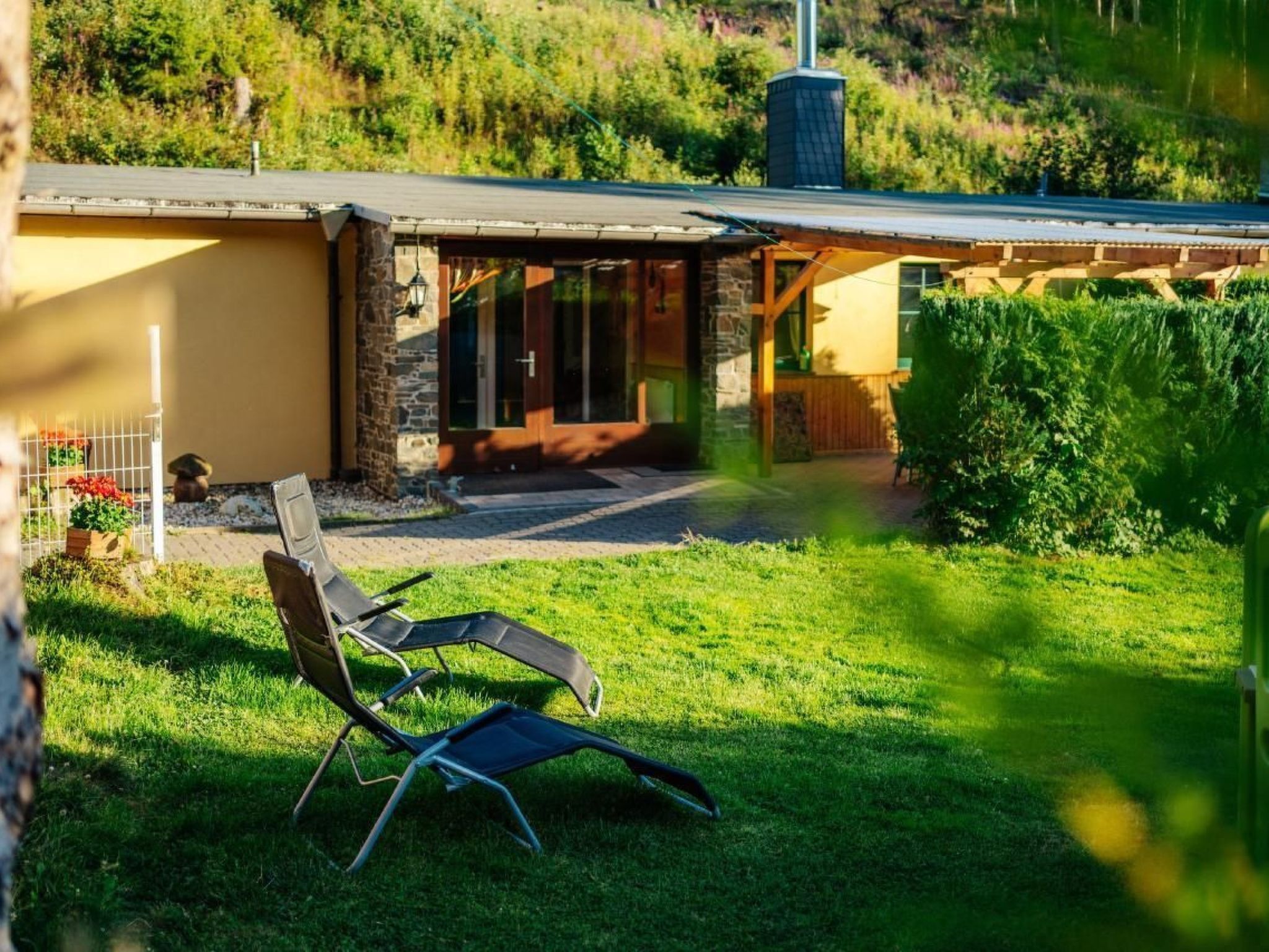 A house with a stone exterior, a covered patio, and a lawn with two lounge chairs.