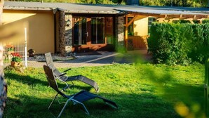 A house with a stone exterior, a covered patio, and a lawn with two lounge chairs. - Vacation home Zita by Interhome (Thale)