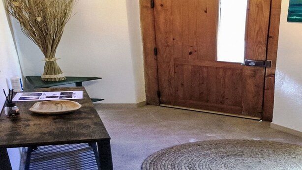 Una puerta de madera, una mesa con un jarrón y una alfombra en una habitación con paredes blancas.