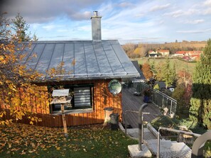 Una baita di legno con tetto in metallo, un piccolo patio e vista su un paesaggio rurale.