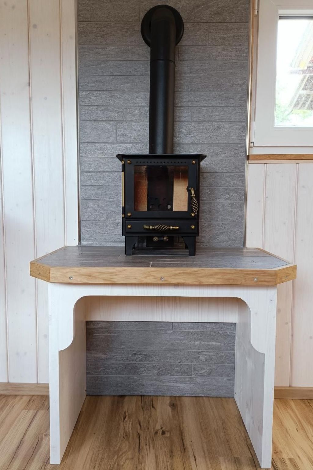 A wood-burning stove with a black chimney, placed on a white bench with a wooden top.
