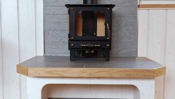A wood-burning stove with a black chimney, placed on a white bench with a wooden top.