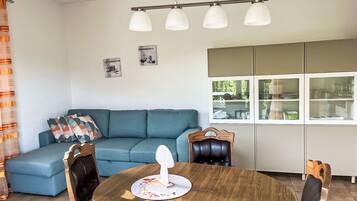 Ein modernes Wohnzimmer mit einem blauen Sofa, einem Holzespeisetisch mit Stühlen und einer Küchenzeile mit Schränken und einem Fenster.