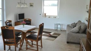 Una sala de estar con un sofá, una mesa de comedor con sillas, un televisor y una ventana con persianas.