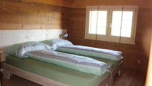 Una habitación tipo cabaña de madera con una cama, una ventana y una mesita de noche.