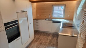 Una cocina compacta con armarios blancos, horno empotrado, lavamanos y ventana sobre la encimera.