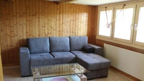 Una habitación con un sofá seccional gris, una mesa de centro de vidrio y suelo de madera.