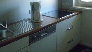 Une cuisine compacte avec des meubles blancs, un lave-vaisselle encastré, une machine à café et une fenêtre qui laisse entrer la lumière naturelle.
