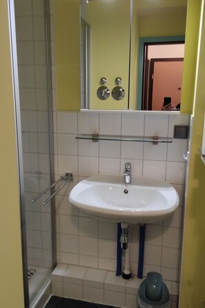 Un baño con lavamanos blanco, un espejo y cabina de ducha.
