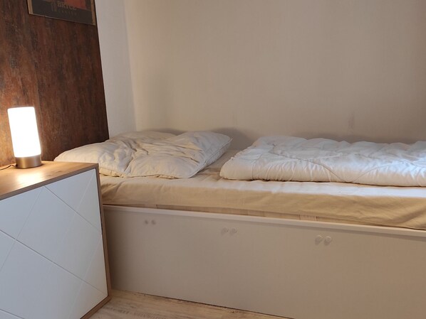 Una cama individual con ropa de cama blanca, una mesita de noche con lámpara y un cabecero de madera.