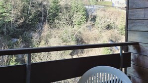 A balcony with a white plastic chair, overlooking a forested area with buildings in the background. - L'Ecrin de Torgon in den Portes du Soleil by Interhome (Torgon)