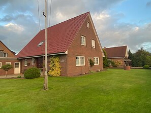 A two-story house with a red-tiled roof, a well-maintained lawn, and a small garden area with a yellow flowering plant. - Geräumige Ferienwohnung mit Garten und Grill by Interhome (Hage)