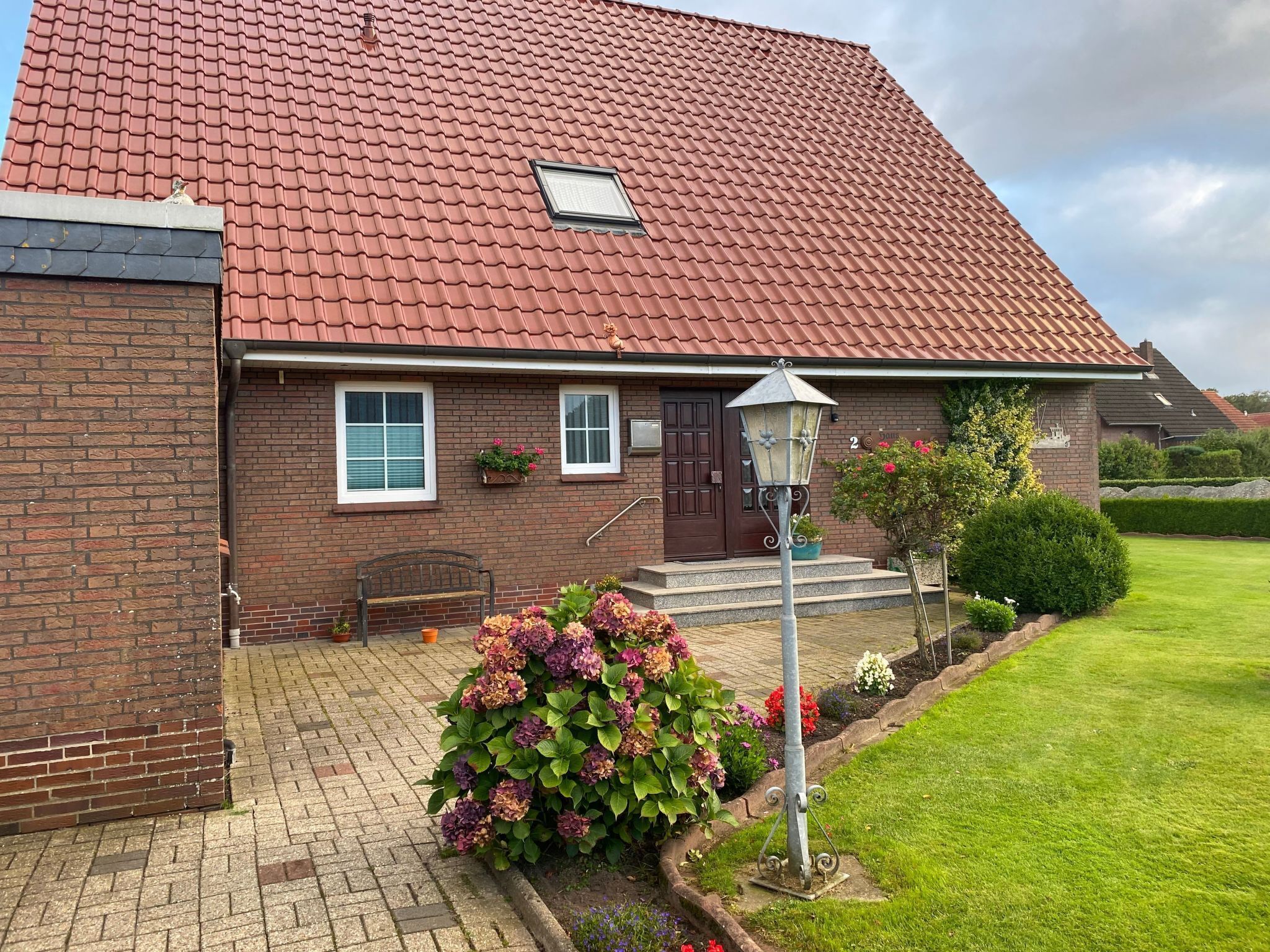 A brick house with a red-tiled roof, a front porch, and a well-maintained garden.