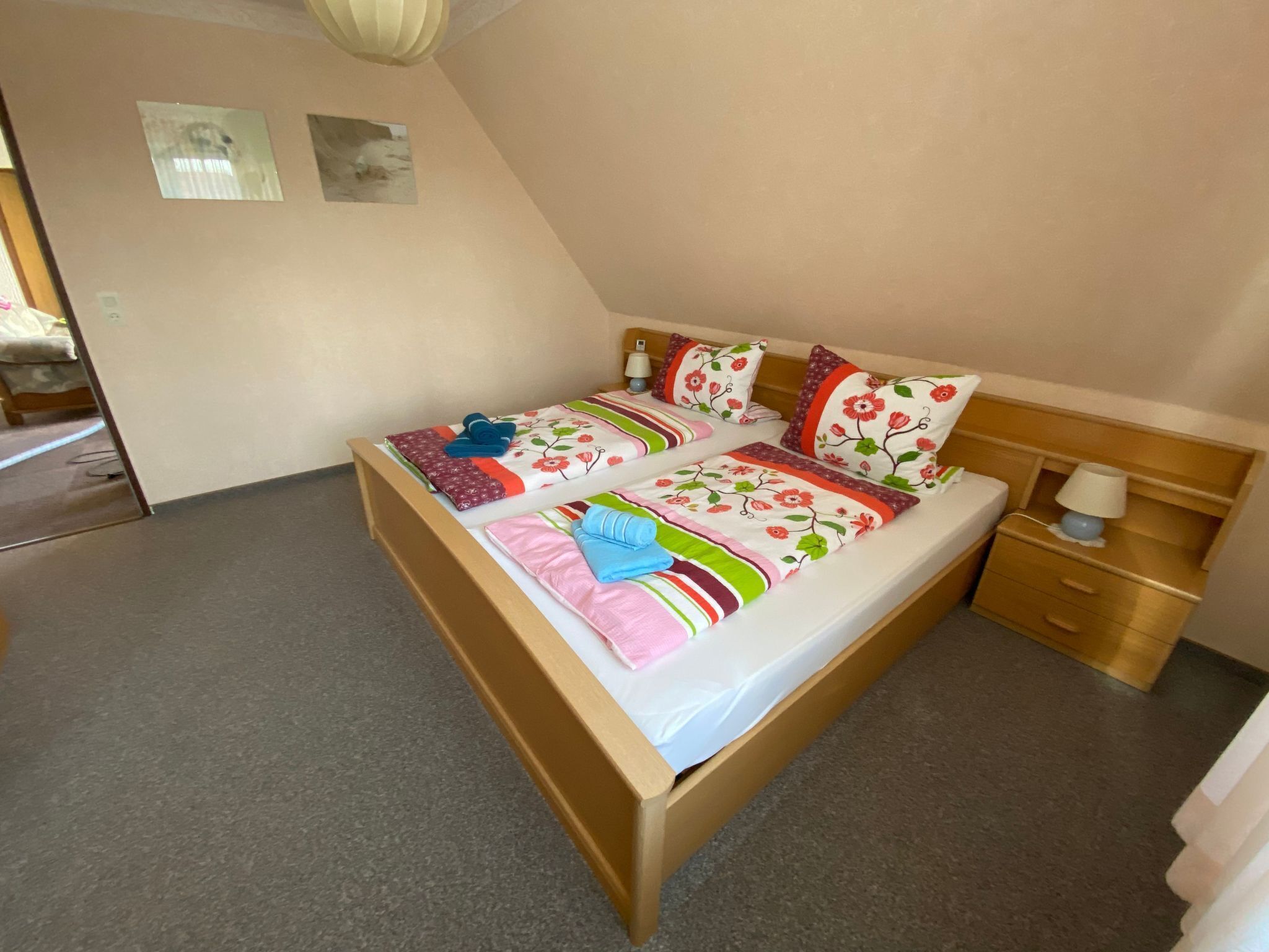 A single bed with a floral bedspread and pillows, a bedside table with a lamp, and a small wooden nightstand.