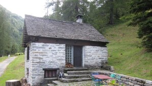 Una cabaña de piedra con un pequeño porche, una mesa y sillas, y un muro de piedra.