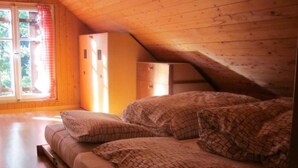 Un dormitorio acogedor en el ático con techo de madera, una cama con ropa de cama estampada, un aparador y una ventana con cortinas.