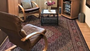 A living room with a brown leather chair, a small table with a vase, a television on a wooden stand, and a patterned rug. - Chalet Adler- Studio für 2 Personen by Interhome (Aminona)