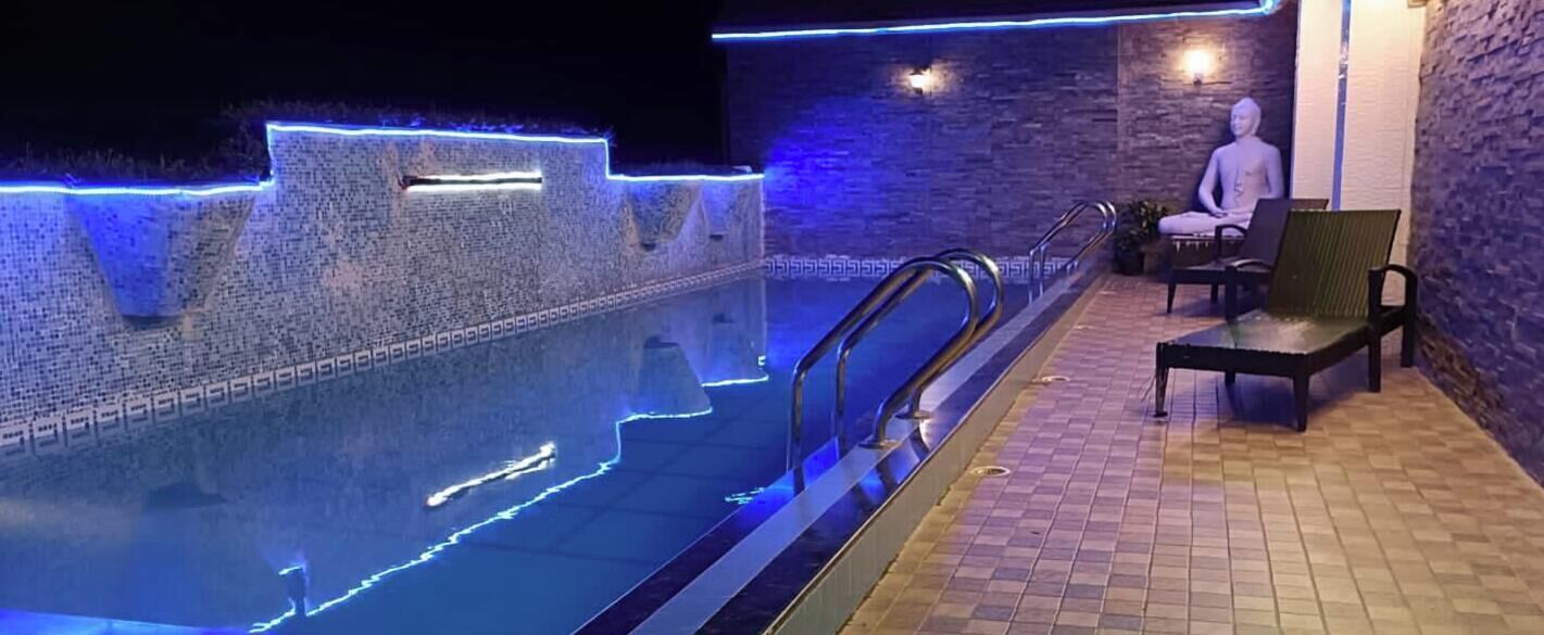 Una piscina con iluminación LED azul a lo largo de los bordes, un muro de piedra y una estatua de Buda.