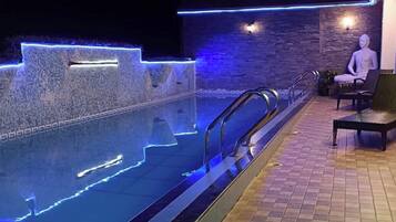 Una piscina con iluminación LED azul a lo largo de los bordes, un muro de piedra y una estatua de Buda.