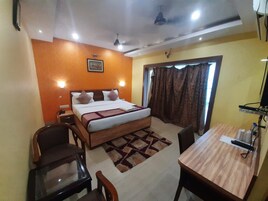 Habitación de hotel con cama, escritorio, dos sillas, ventilador de techo y ventana con cortinas.