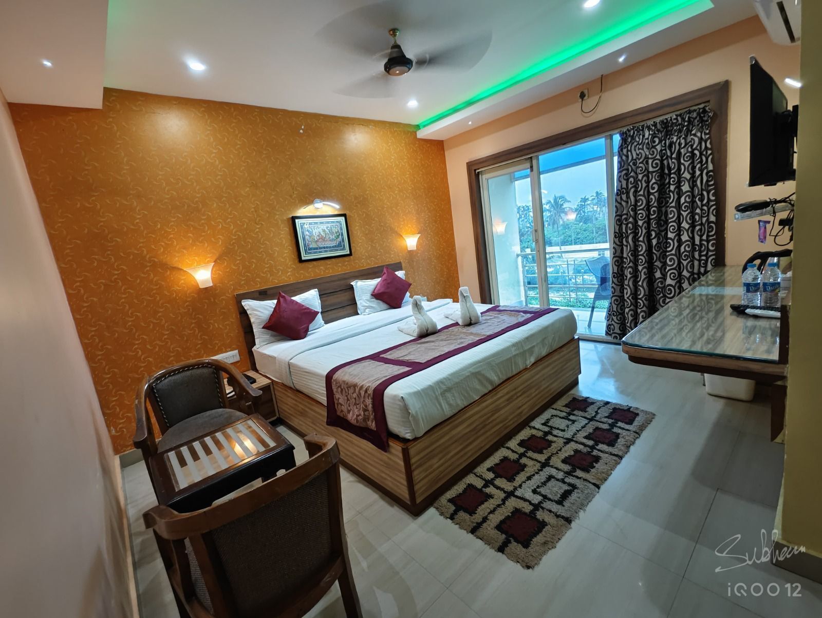 A hotel room with a bed, a desk, a chair, a window with curtains, and a view of the outdoors.
