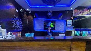 A reception desk with a digital screen displaying a floral design, a clock, and a sign with a phone number.