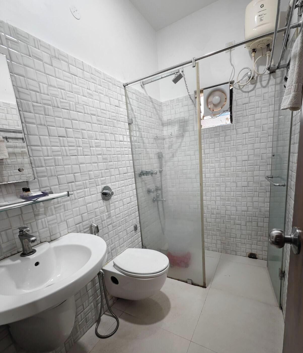 Un baño con lavamanos blanco, inodoro y cabina de ducha con mampara de cristal.