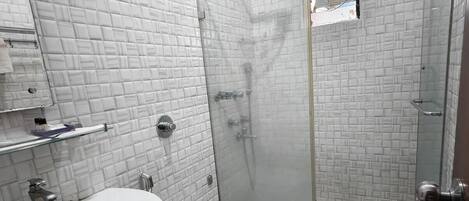 Un baño con lavamanos blanco, inodoro y cabina de ducha con mampara de cristal.