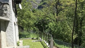 Un bâtiment en pierre doté d’un balcon, une cour verdoyante et une chaîne de montagnes en arrière-plan.